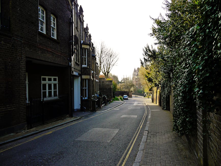 A multi-storey residential building with a modern brick exterior and large windows, situated along a quiet street in West Hampstead. The ground floor has a landscaped boundary with shrubs and small pl