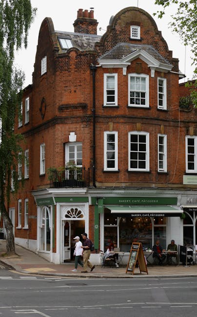 A narrow residential street in West Hampstead with cobbled pavement and a slight incline, lined with brick and stone houses, some with bay windows and external lighting fixtures. A white bay-fronted b