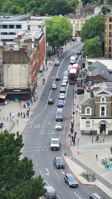 A narrow, sloped street in West Hampstead with brick and stone buildings on either side. On the left, a building with a sign reading 'The Holly Bush' features a white bay window and hanging flower bas