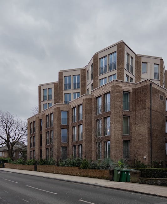 Photograph of a street scene in West Hampstead with a large multi-storey residential building featuring multiple windows, some with white window frames, and a rounded corner section at the top. Severa