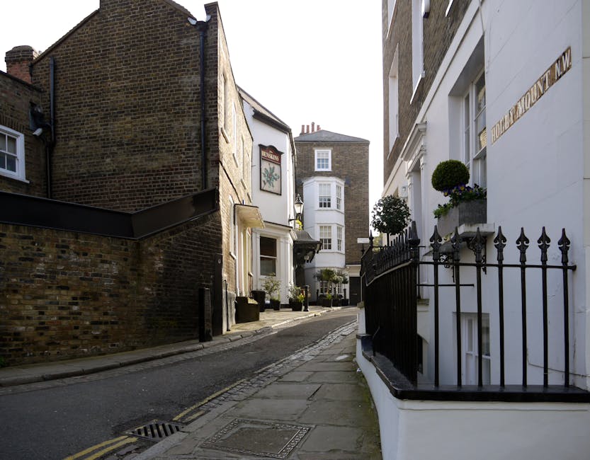 A row of white terraced houses on a cobblestone street in West Hampstead, with each property featuring blue-painted garage doors and external stairs leading to small balconies with black metal railing